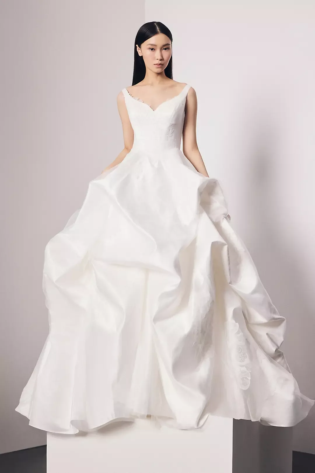 A woman in a white wedding gown with a full skirt and fitted bodice, standing against a plain background.