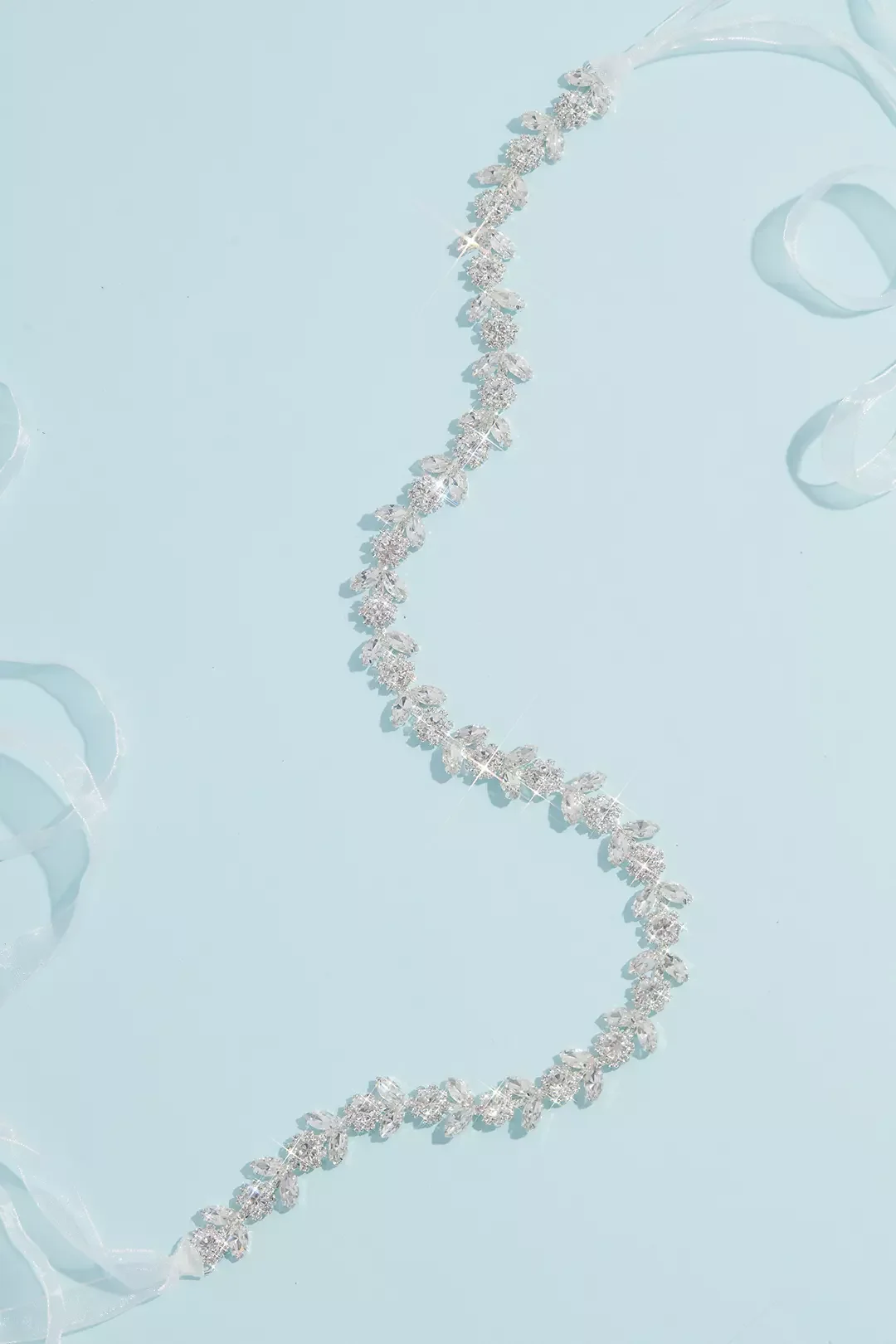 Silver tiara with intricate floral design resting on light blue background with ribbon curls.