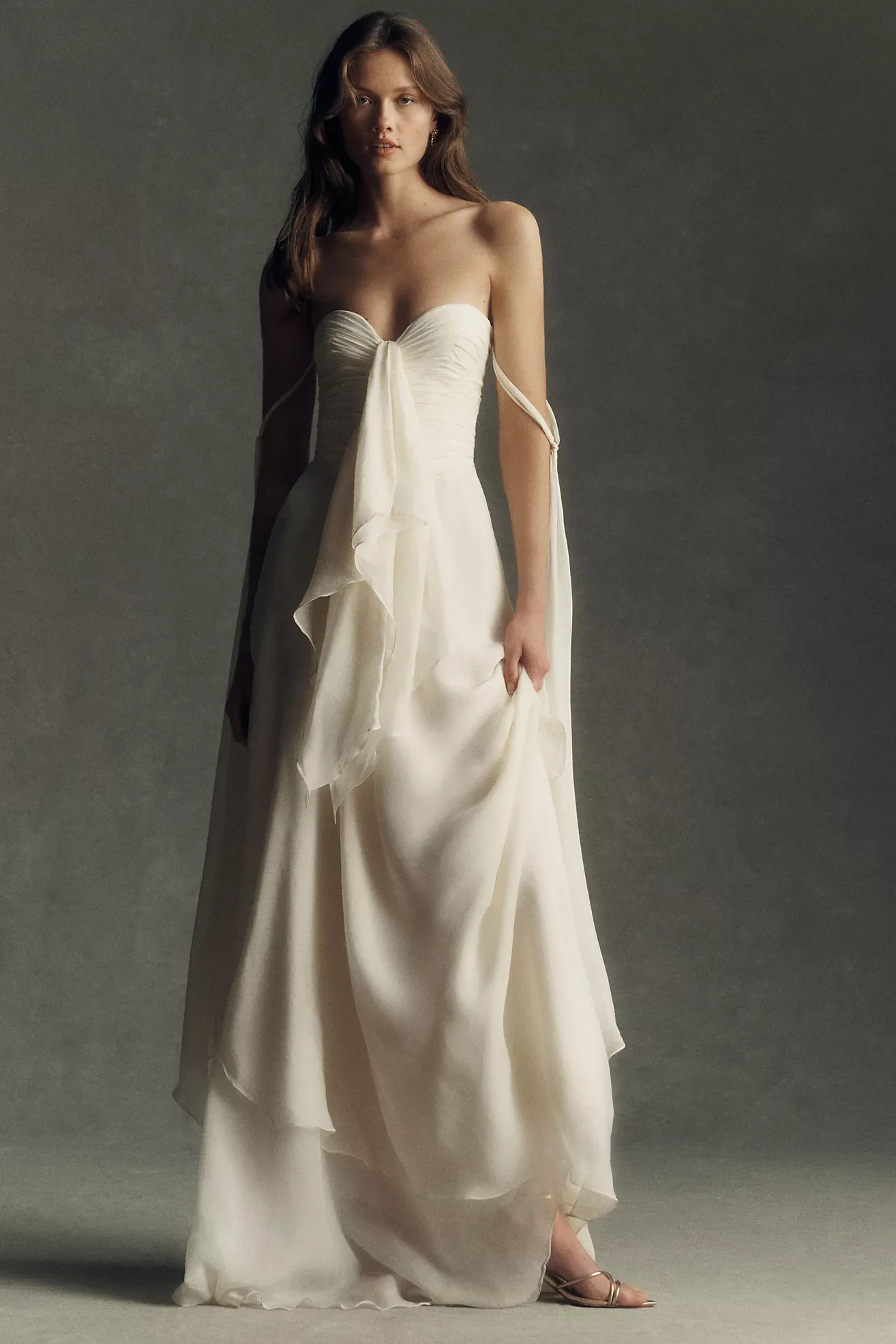 A woman in a strapless white gown with a bow at the bust, standing against a plain background.