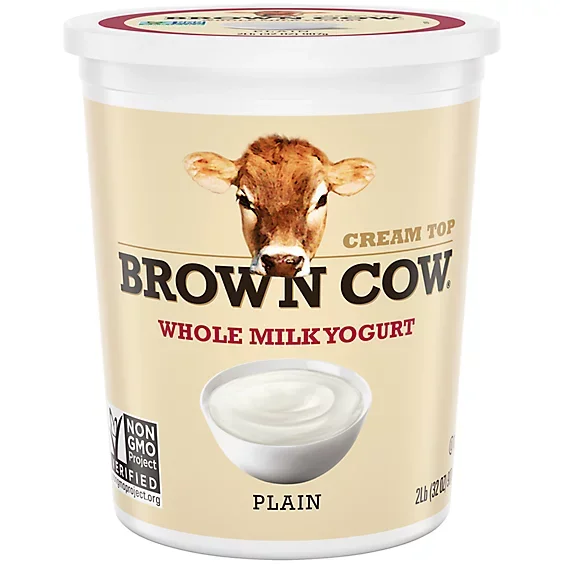 A 2-liter tub of Brown Cow cream top whole milk yogurt featuring a cow's face on the label, with a bowl of plain yogurt and a Non-GMO Project Verified seal.
