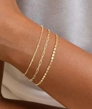 A person's arm wearing three gold bracelets with different chain styles.