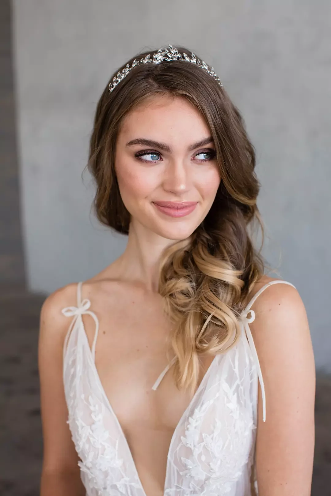 A young woman with long, wavy brown hair and blue eyes wearing a white dress with thin straps and a silver tiara.