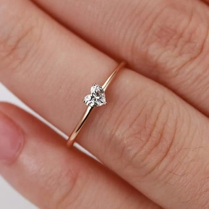 Close-up of a hand wearing a delicate gold ring with a small heart-shaped diamond.