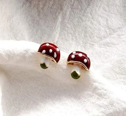 Pair of red mushroom-shaped earrings with white dots on a white fabric background.
