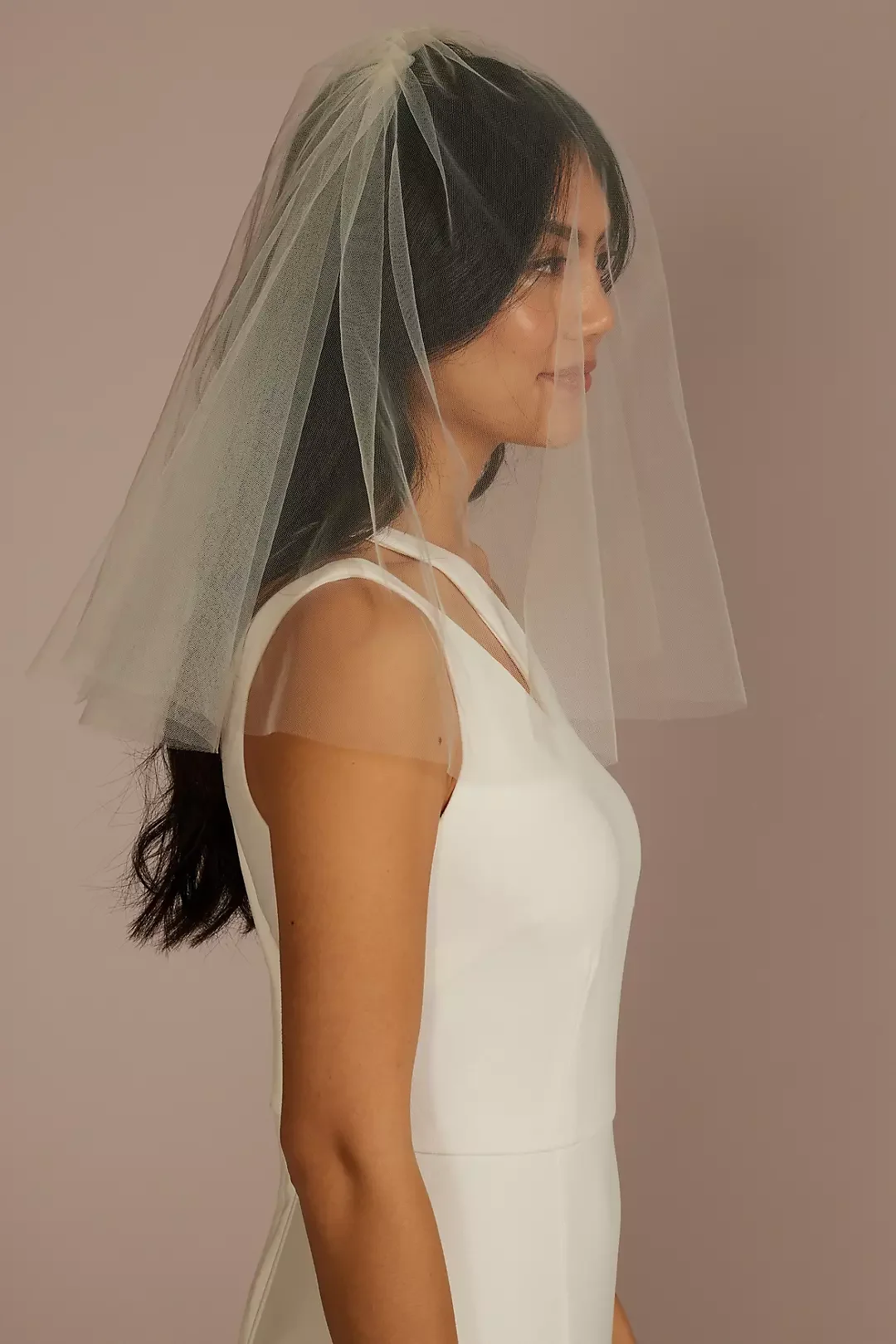 A woman wearing a white sleeveless dress with a veil on her head, standing in profile against a plain background.