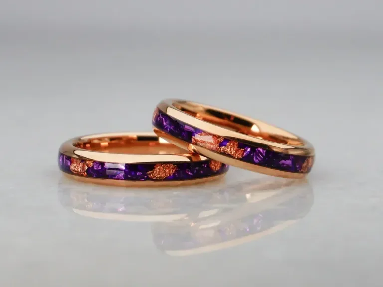 Two rose gold rings with purple and rose gold accents, placed on a reflective surface.