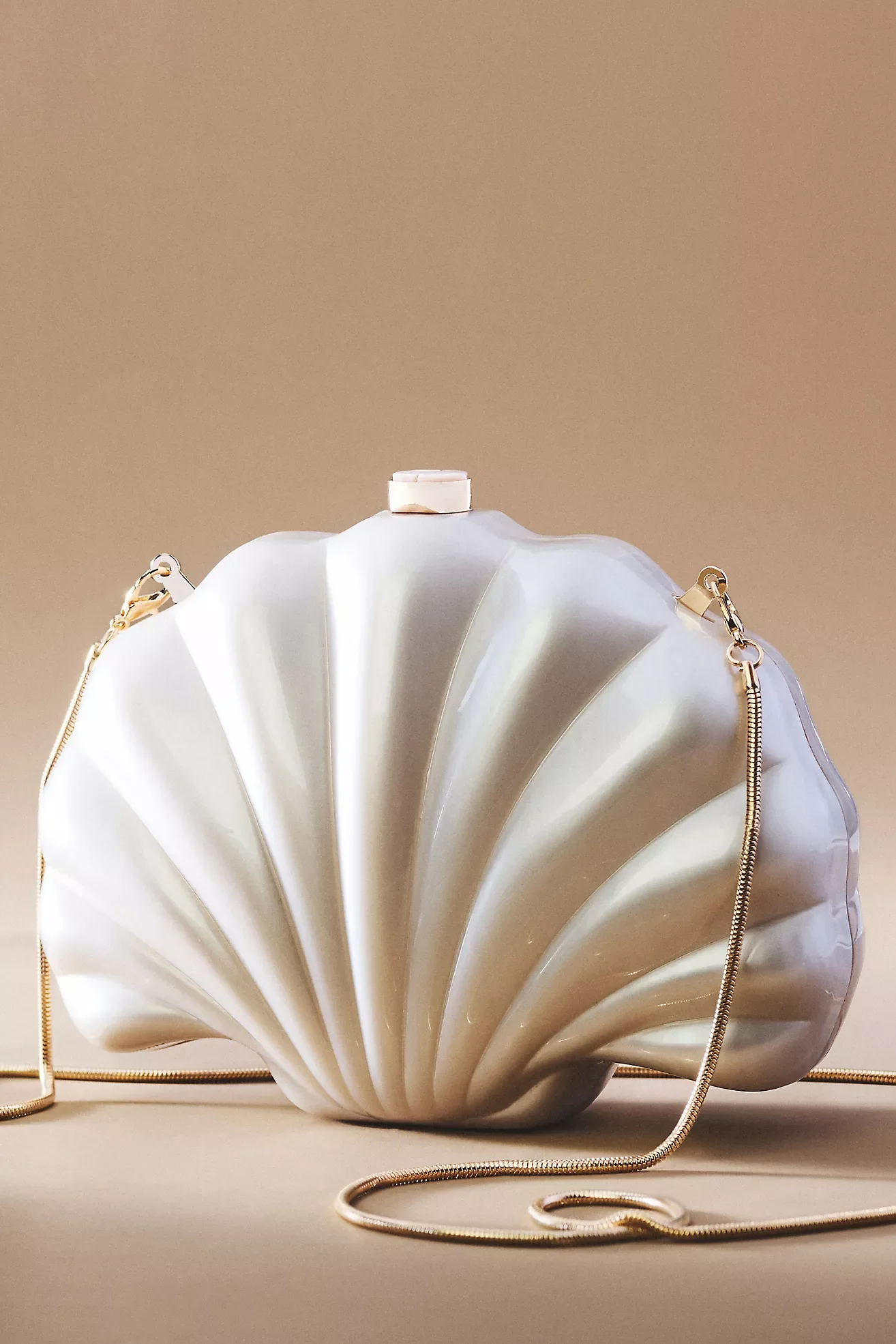 A white seashell-shaped handbag with gold chain straps on a plain surface with a neutral background.