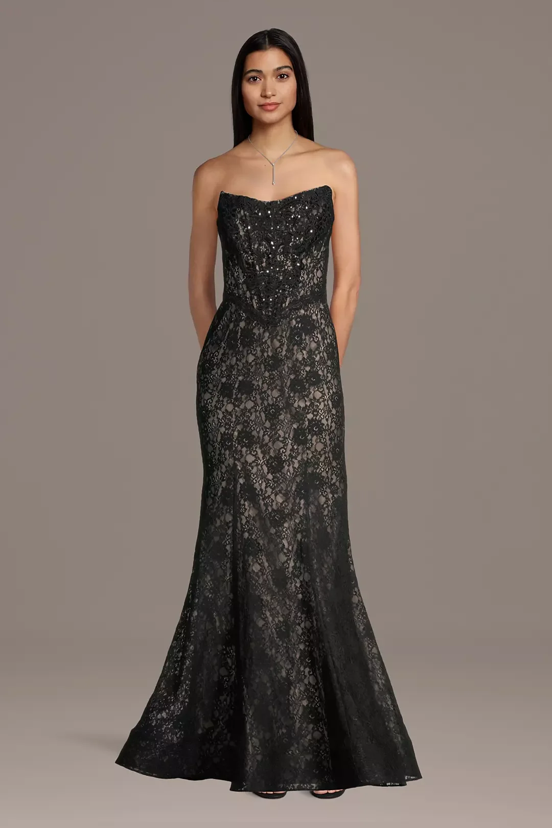 A woman wearing a strapless, black lace evening gown with a fitted bodice and a long, flowing skirt.