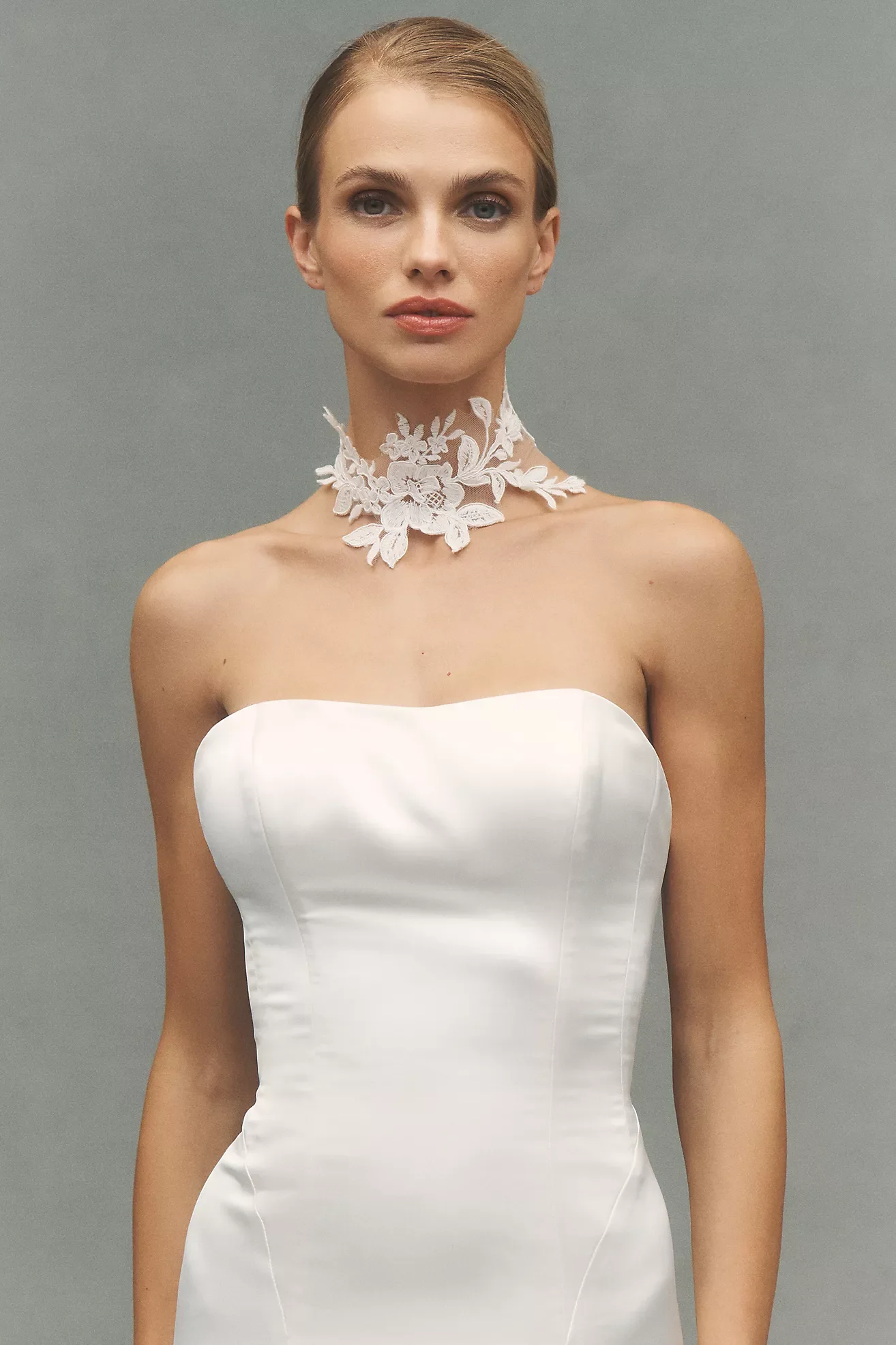 A woman wearing a strapless white wedding dress and a white lace floral choker necklace.