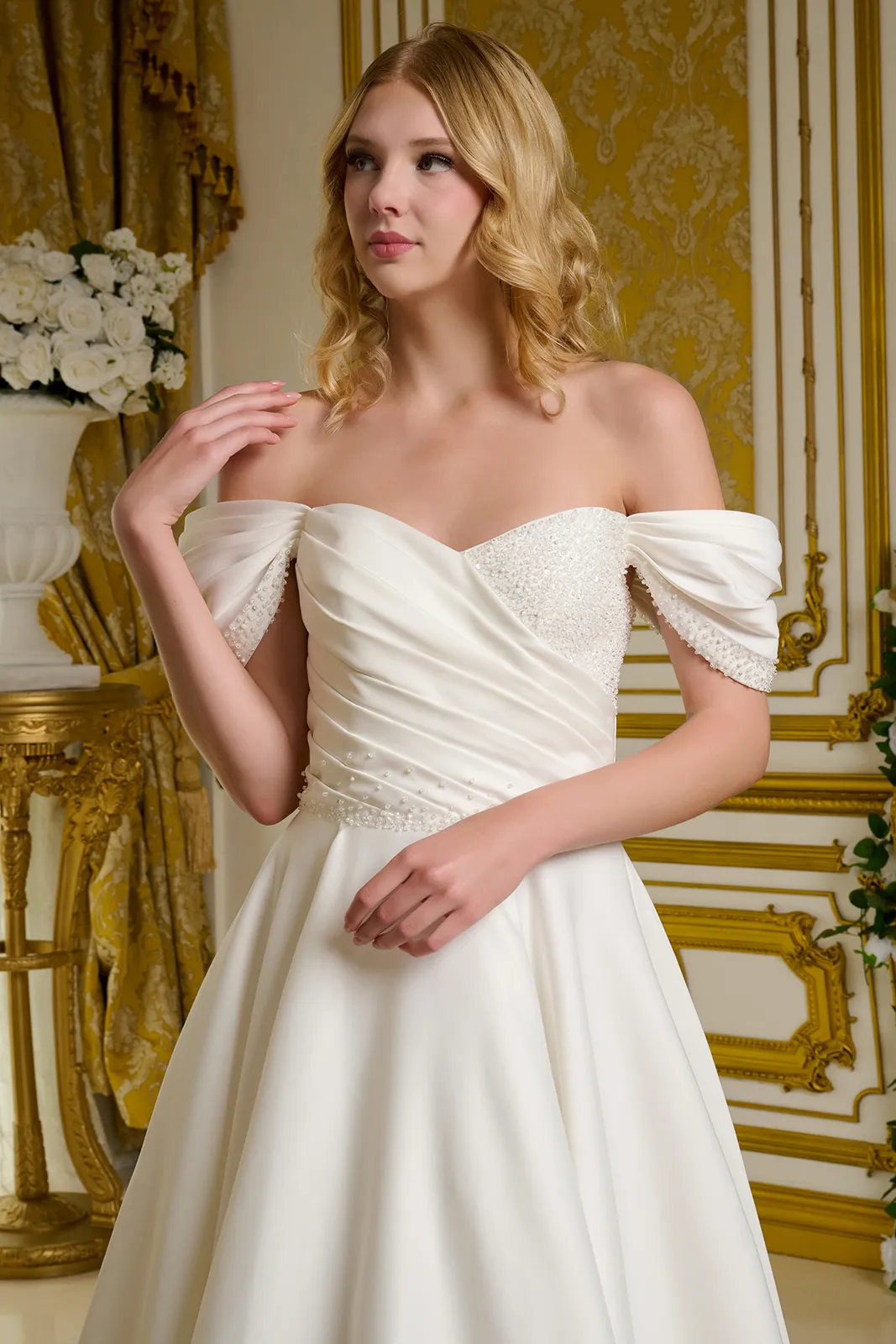 A woman in a wedding dress standing in a decorated room with gold accents and white floral arrangements.
