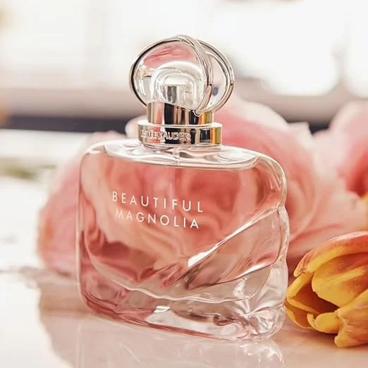 A bottle of perfume labeled 'Beautiful Magnolia' placed on a surface with pink flowers in the background.