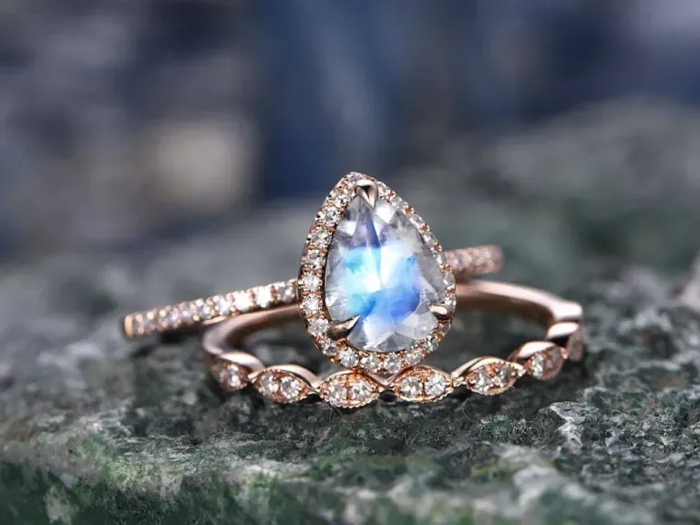 Two delicate rings with diamond accents, one featuring a teardrop-shaped gemstone, resting on a textured surface.