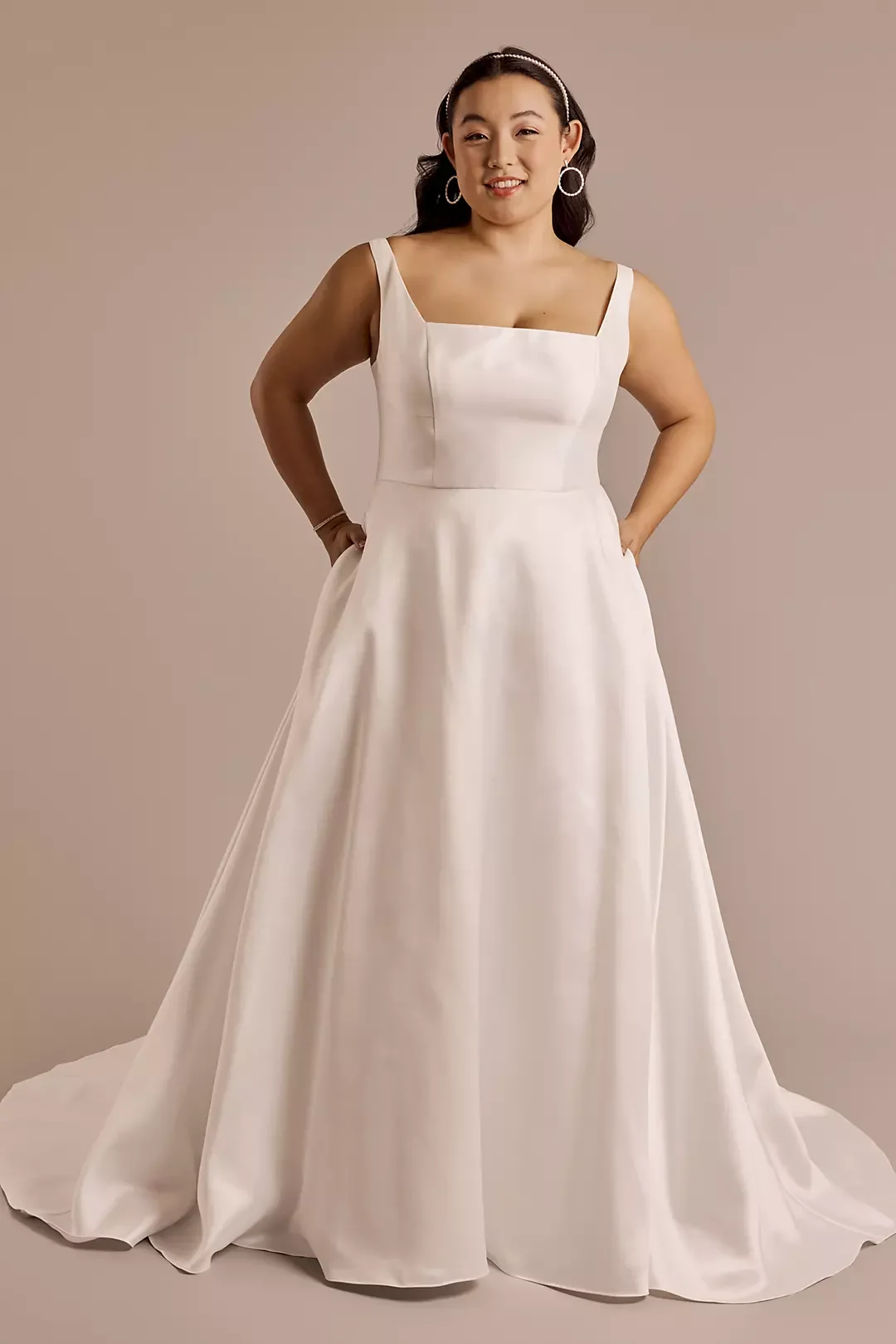 A woman wearing a sleeveless white gown with a fitted bodice and full skirt, posing against a plain beige background.