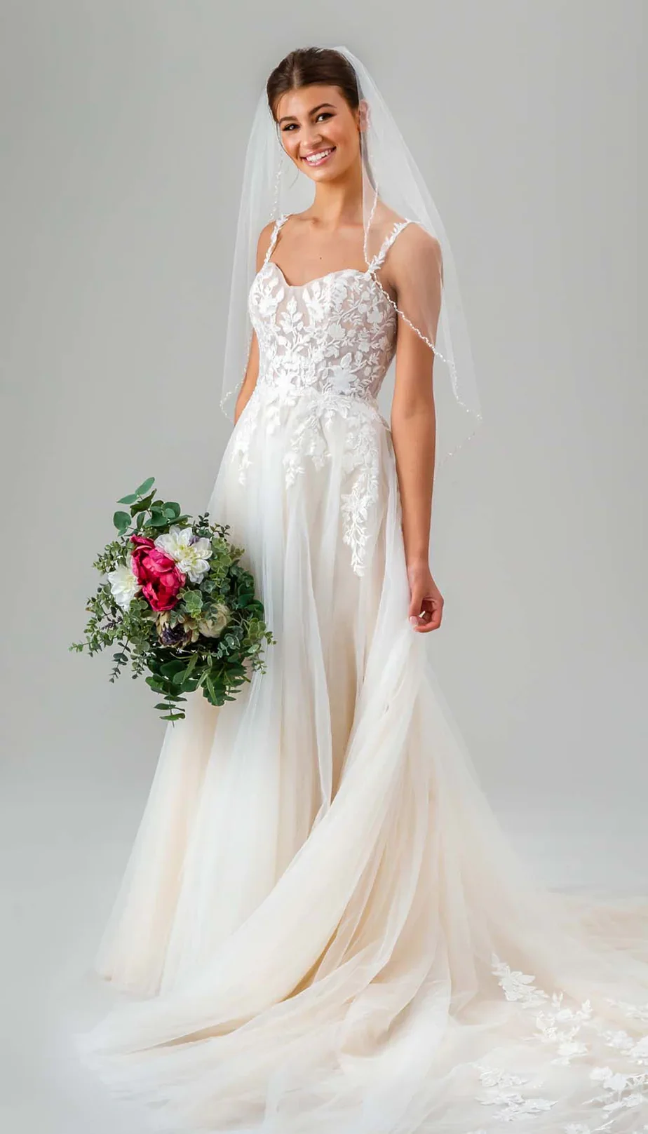 A smiling woman in a wedding dress holding a bouquet of flowers.