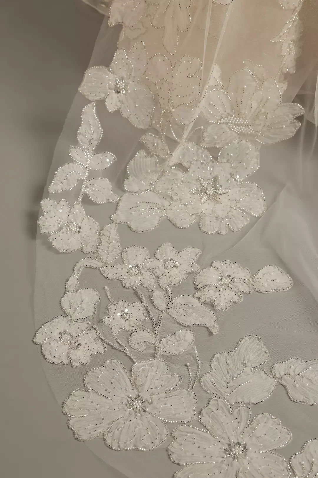 Close-up of white lace fabric with floral embroidery and bead embellishments, likely part of a wedding dress or veil.