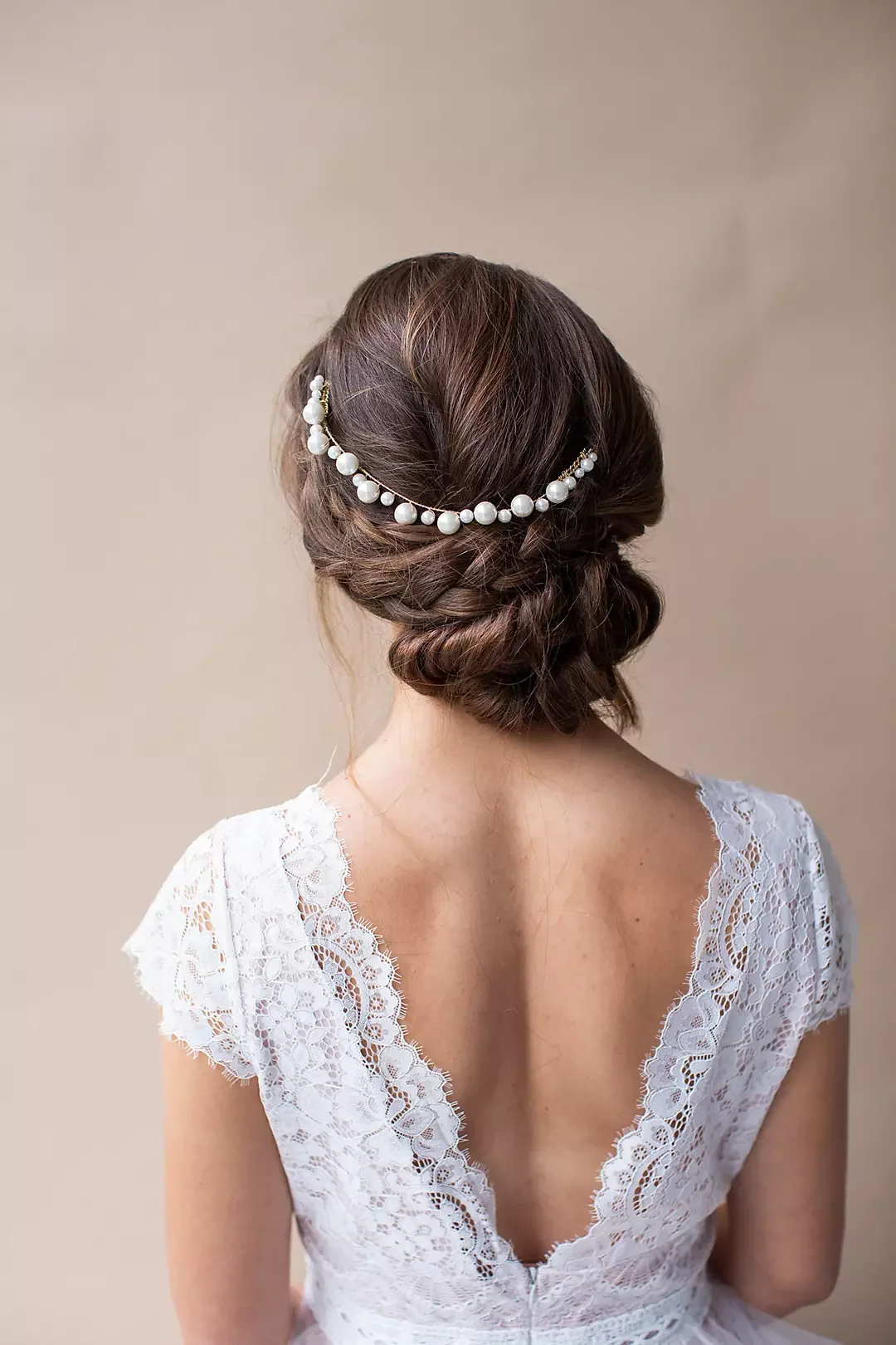 Back view of a woman with styled brown hair wearing a pearl hair accessory and a white lace dress.