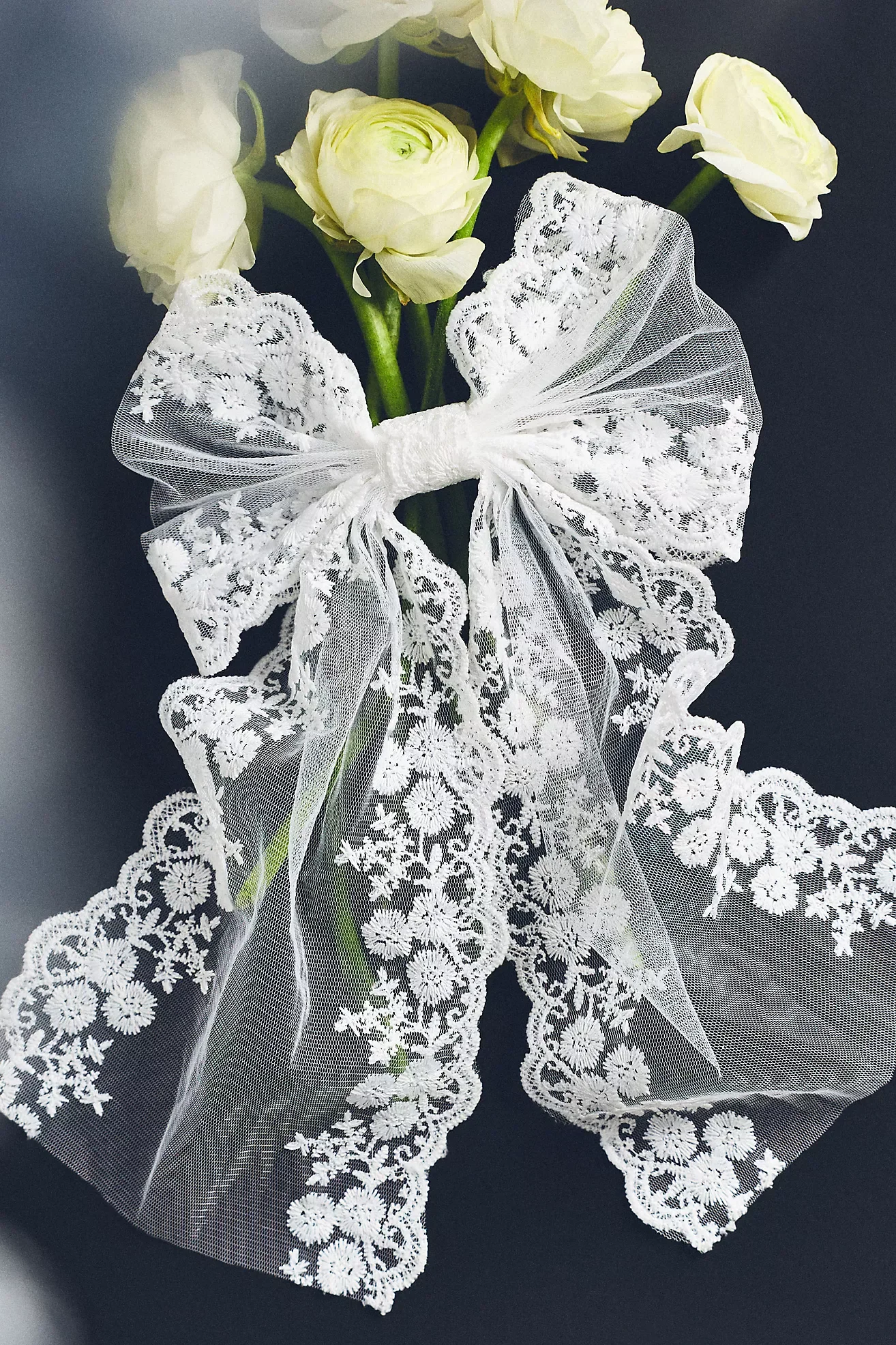 White flowers with lace and sheer ribbons on a dark background.