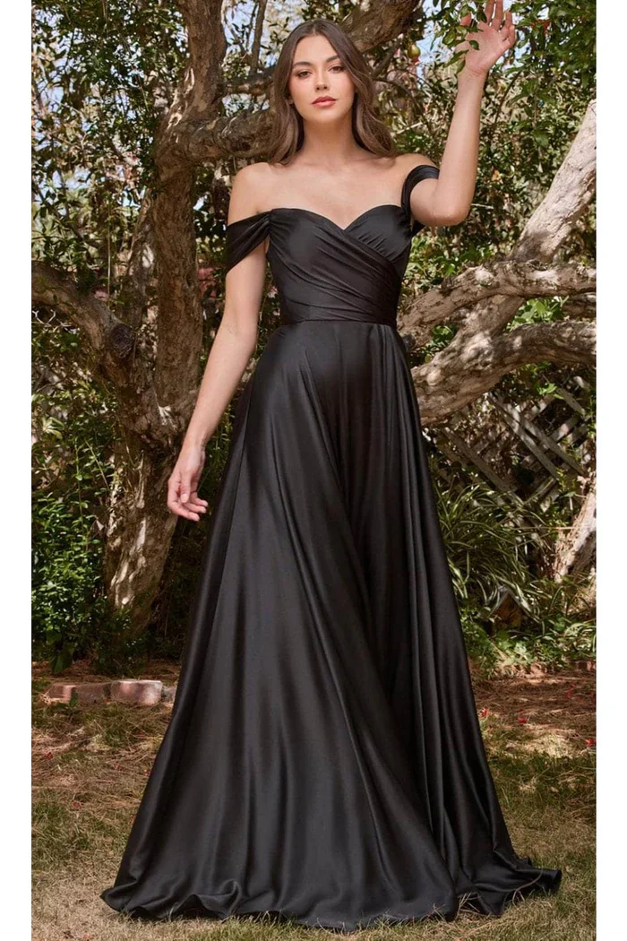 A woman wearing a long, black off-shoulder evening gown standing outdoors near a tree.