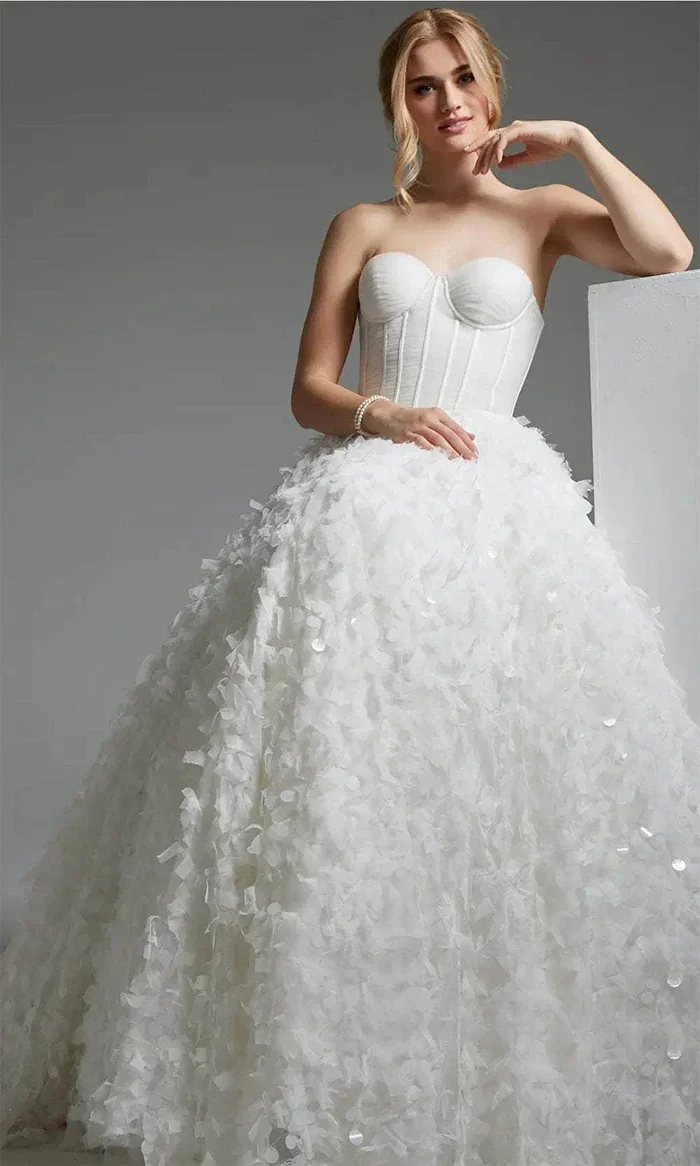 A woman wearing a strapless white wedding gown with a textured, fluffy skirt and structured bodice, posing against a gray background.