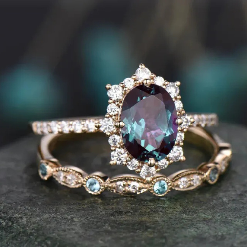 Close-up of an oval-cut dark gemstone surrounded by small diamonds and a delicate gold band with blue gemstones.