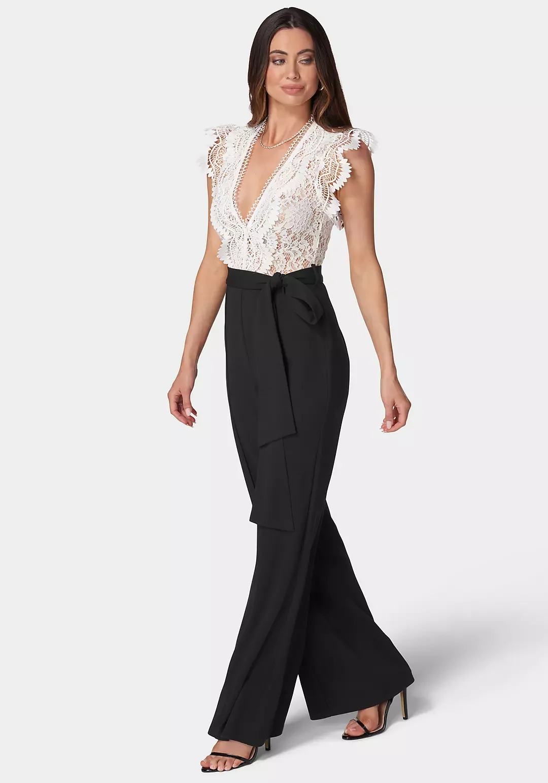 Woman wearing a white lace top with ruffled sleeves and a deep V-neck, paired with high-waisted black wide-leg pants with a bow tie at the waist.