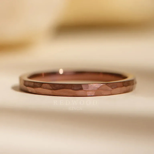 Close-up of a rose gold hammered wedding band on a pale surface with blurred background.