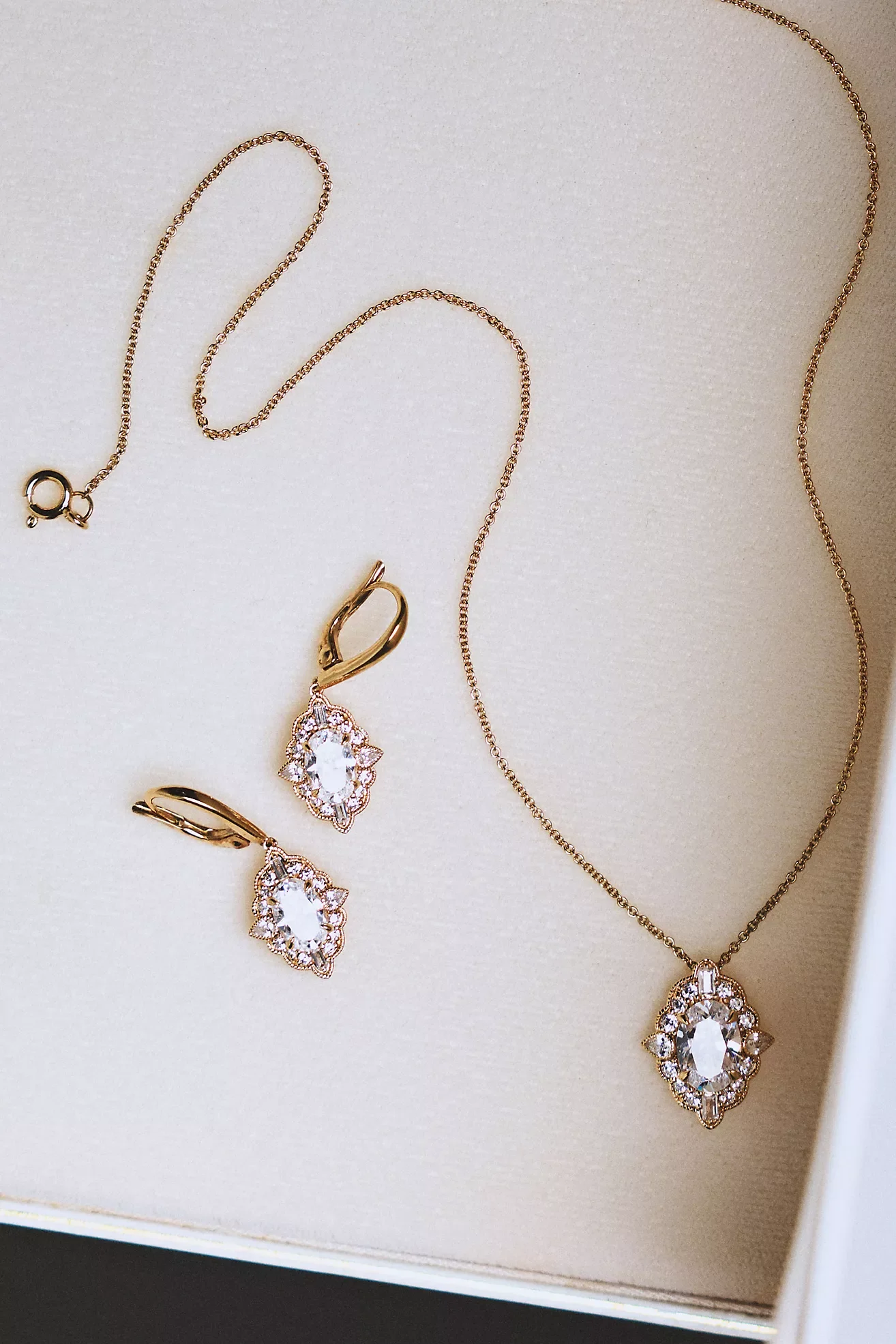Jewelry display with gold necklace, matching earrings, and a pendant necklace with large clear gemstones.