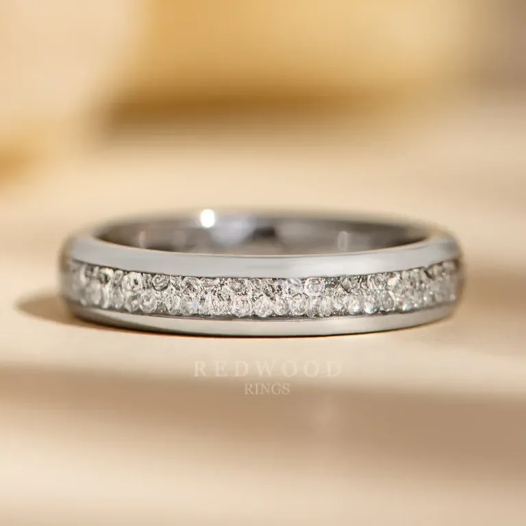 Silver ring with small diamonds embedded along the top edge, resting on a wooden surface.