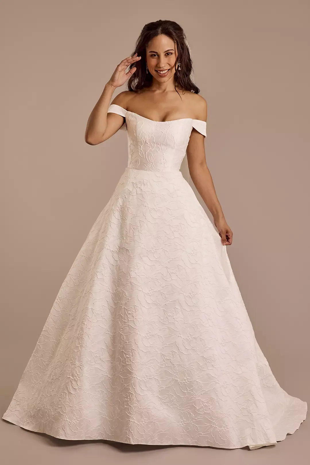 Woman in wedding dress smiling and posing against a beige background.