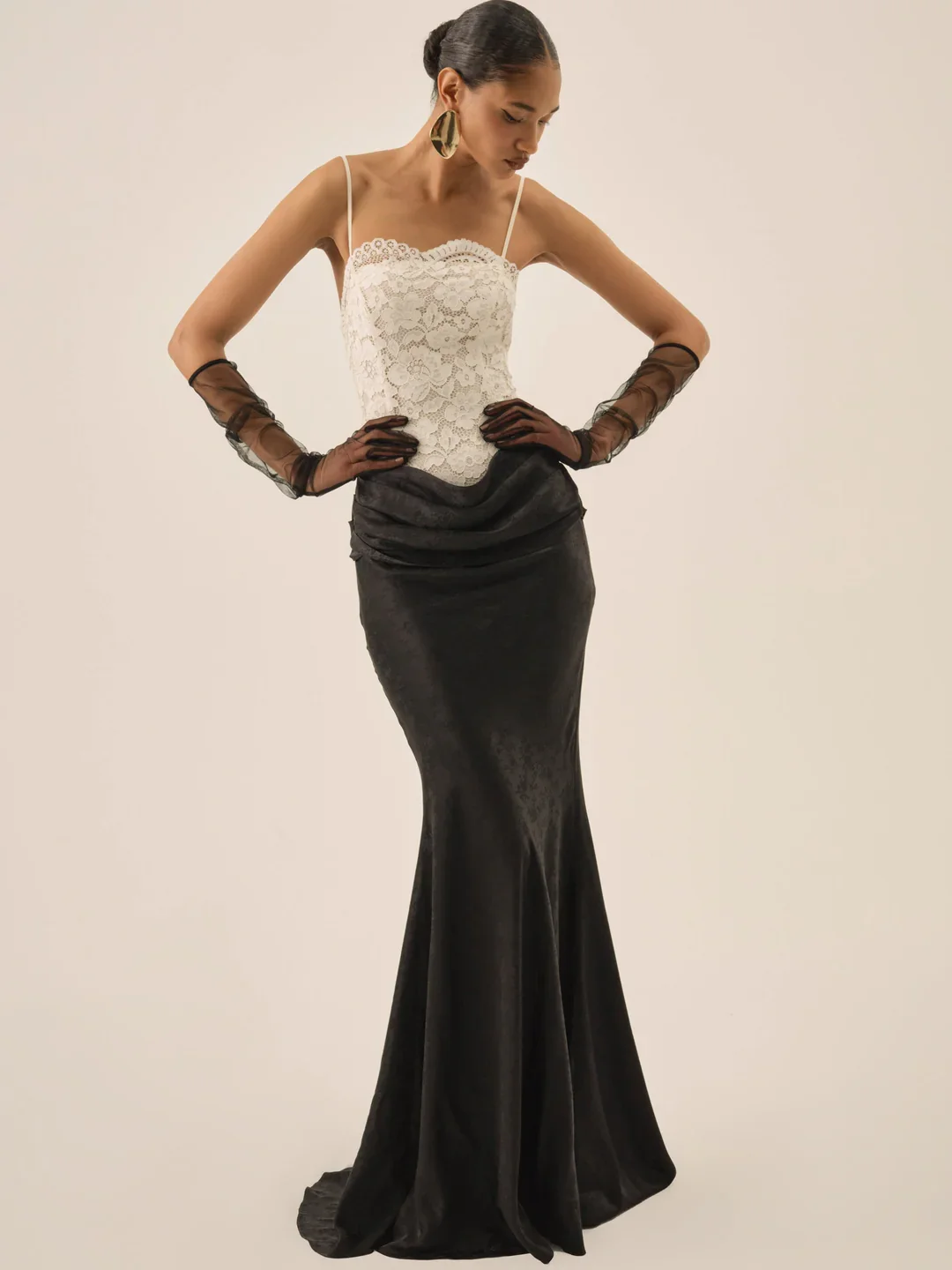 A woman in a black floor-length skirt, white lace top, and sheer black gloves, posing against a neutral background.