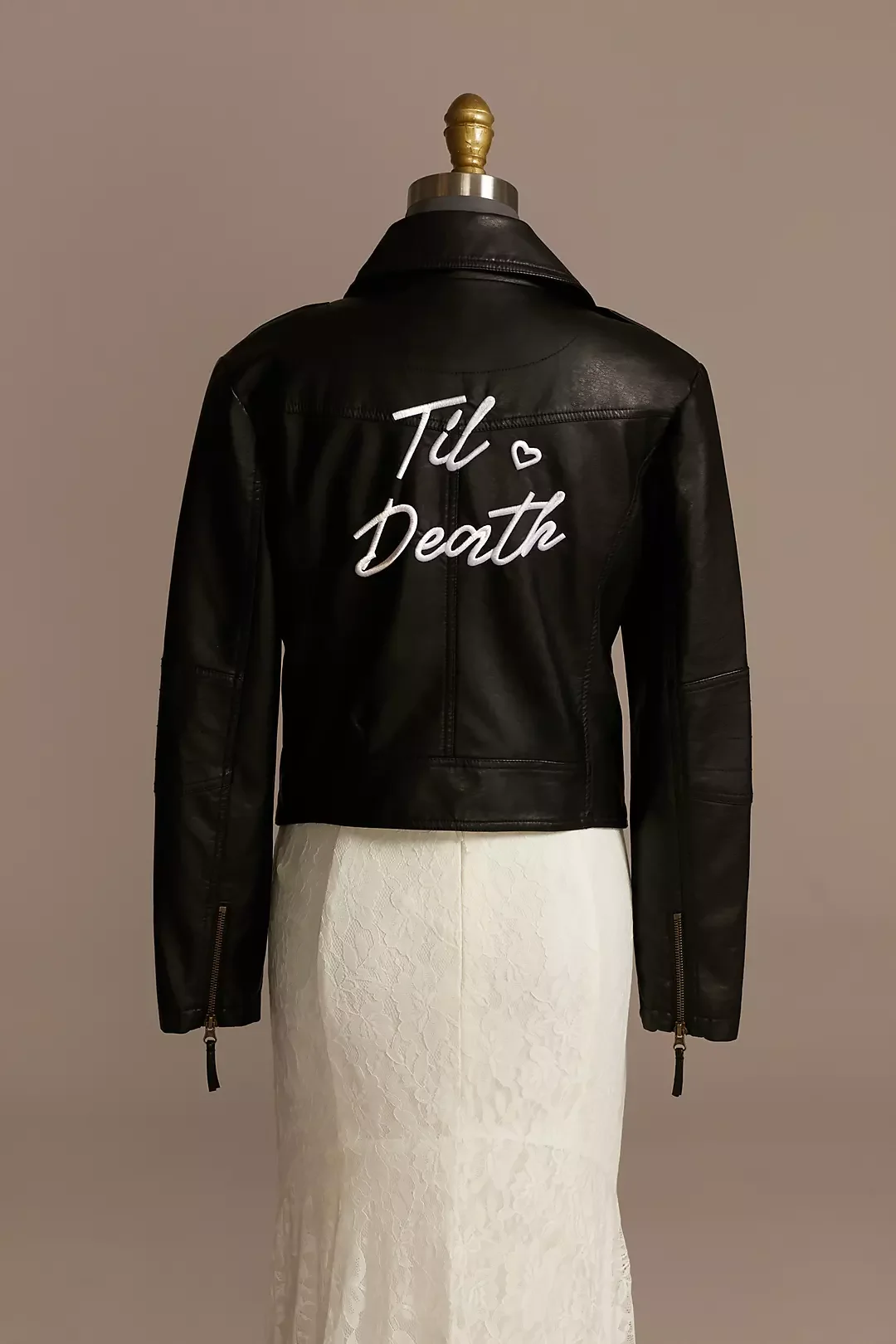 Black leather jacket with white embroidered text reading 'Till Death' and a small heart symbol, displayed on a mannequin with a beige background.