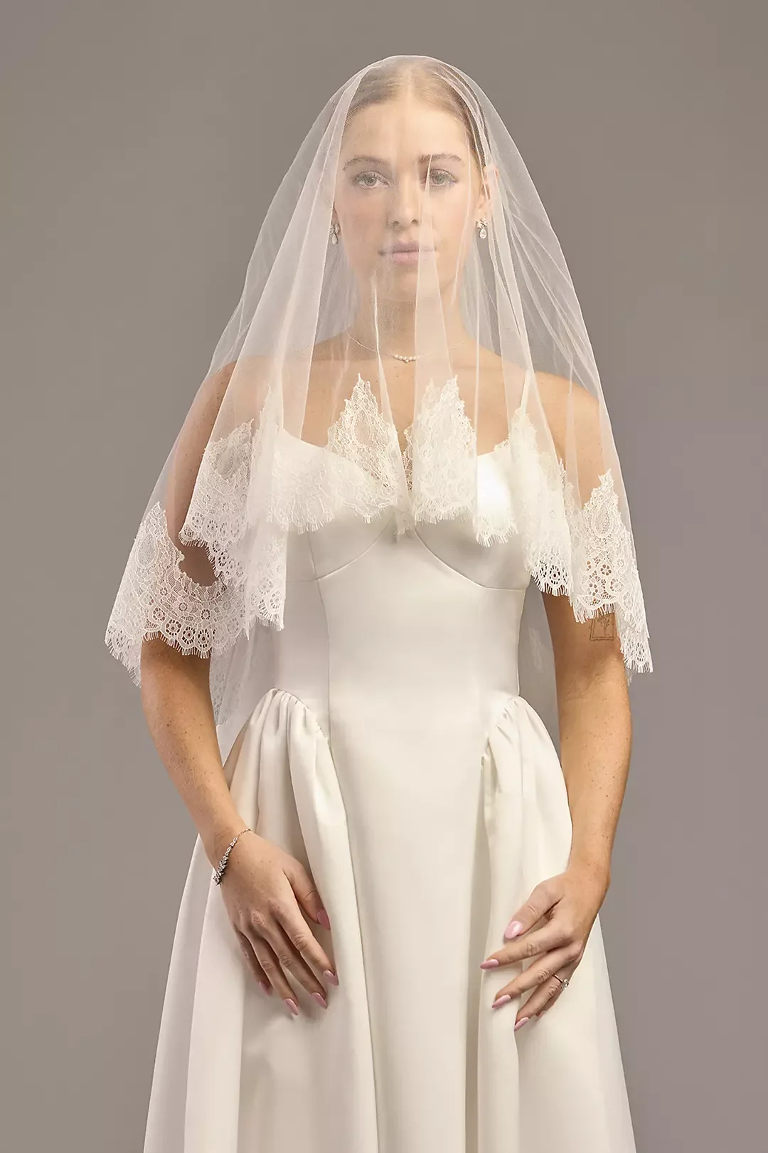 A woman in a wedding dress with lace details on the sleeves and a veil.
