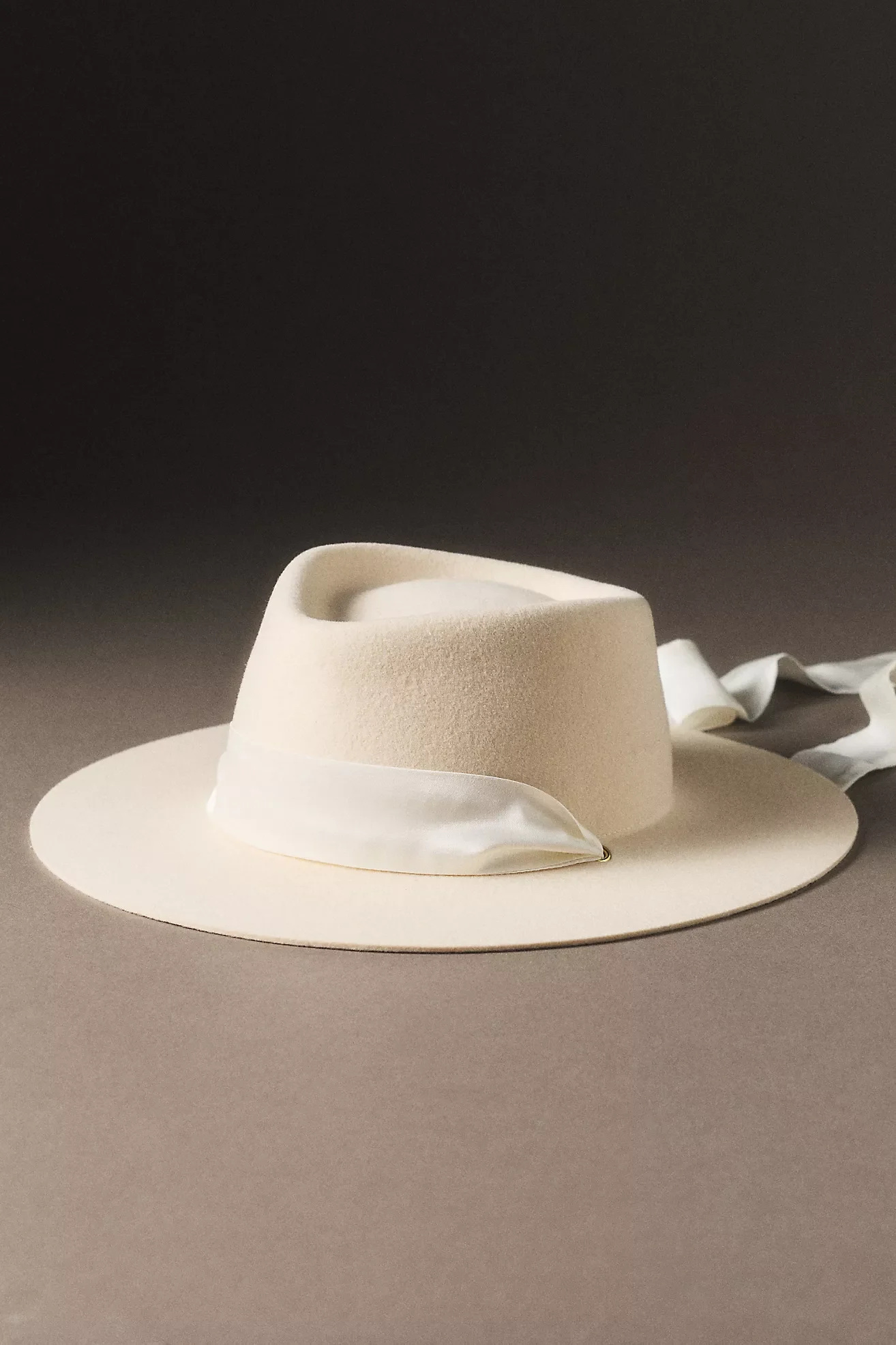 A beige wide-brimmed hat with a decorative white band, placed on a smooth surface, against a dark background.