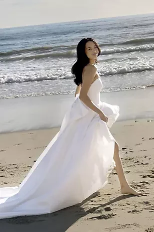 A woman in a white gown standing on the beach with waves in the background.