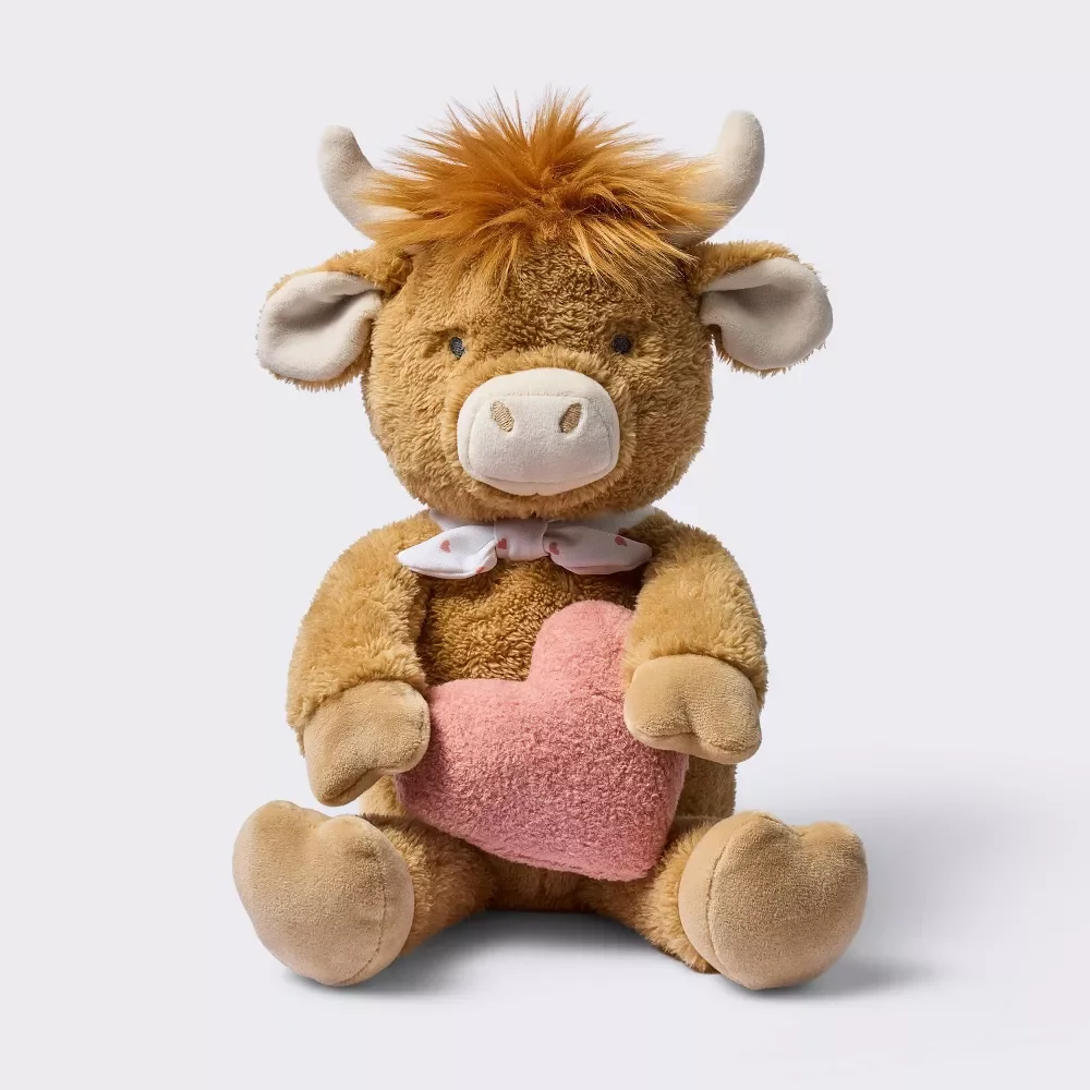 Stuffed animal resembling a cow holding a pink heart.