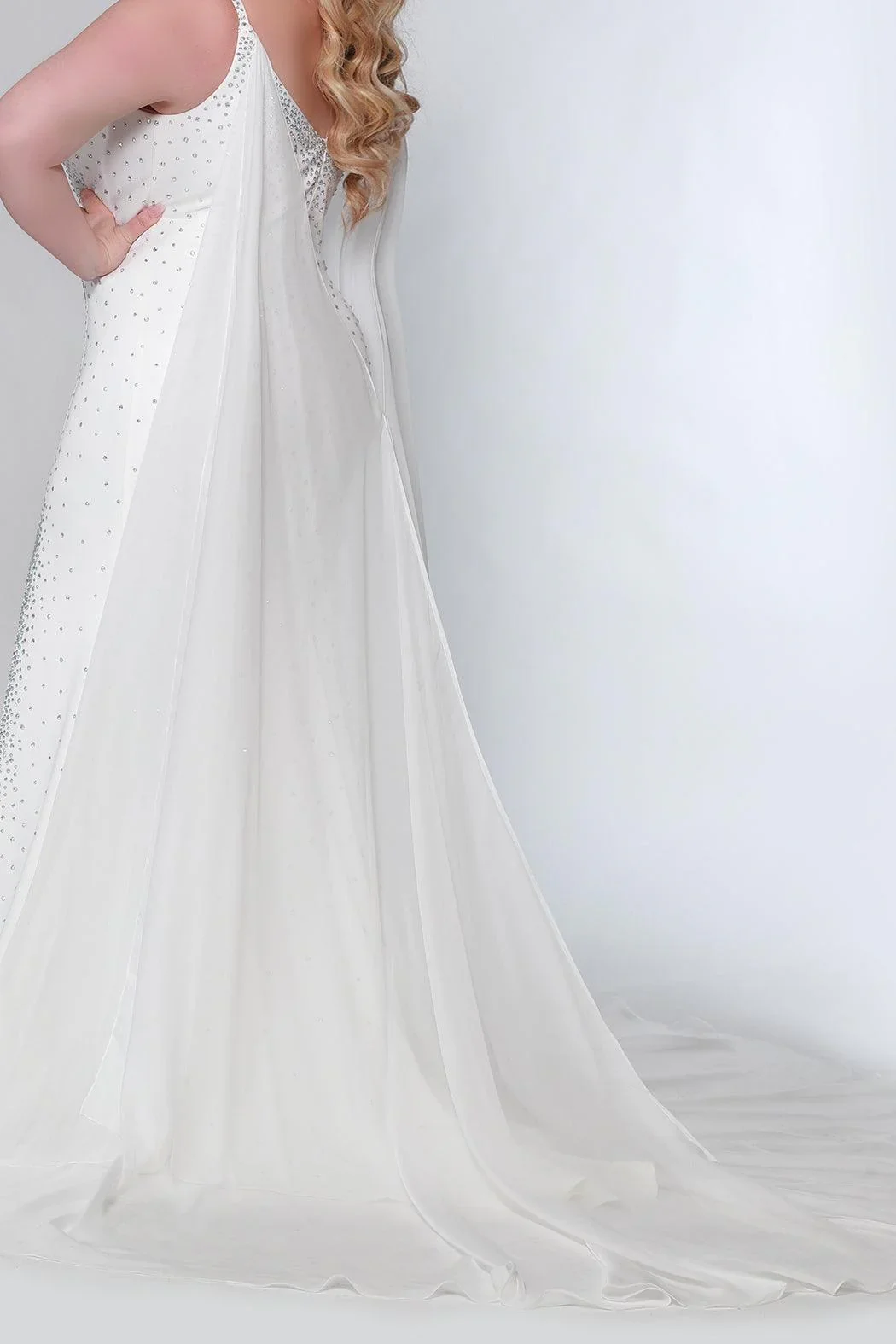 Close-up of a person in a white wedding dress with decorative embellishments, standing against a plain light background.