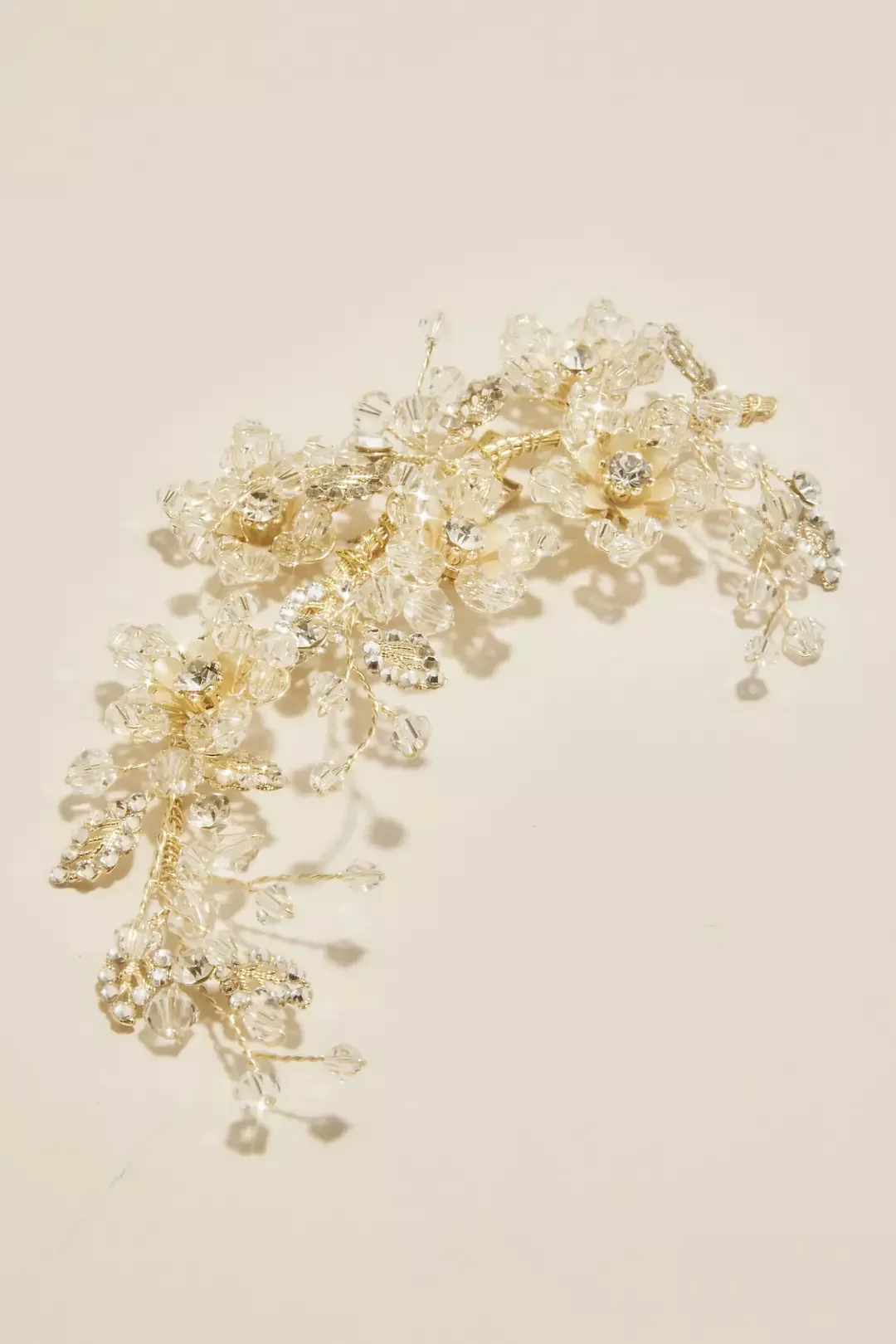 A decorative jewelry piece resembling a floral or branch design with gold-colored metal and clear, sparkling gemstones or crystals.