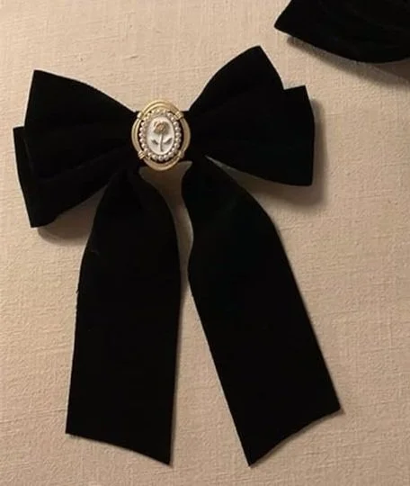 Black velvet bow with a decorative brooch in the center, hanging on a beige wall.
