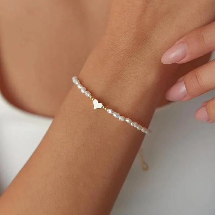 Close-up of a woman's wrist wearing a pearl bracelet with a small gold heart charm.