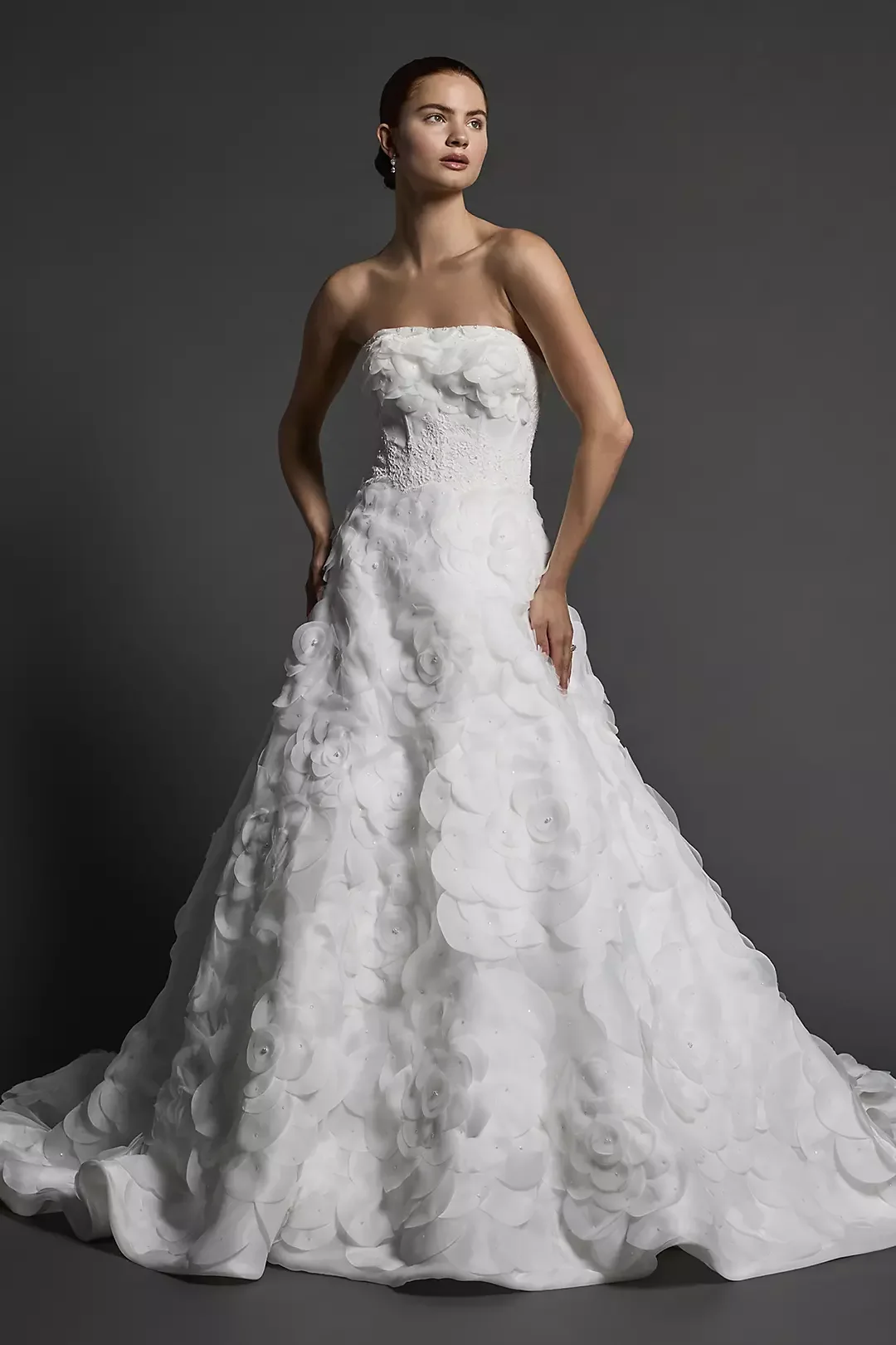 A woman wearing a strapless white wedding gown with floral textured fabric and a long train.