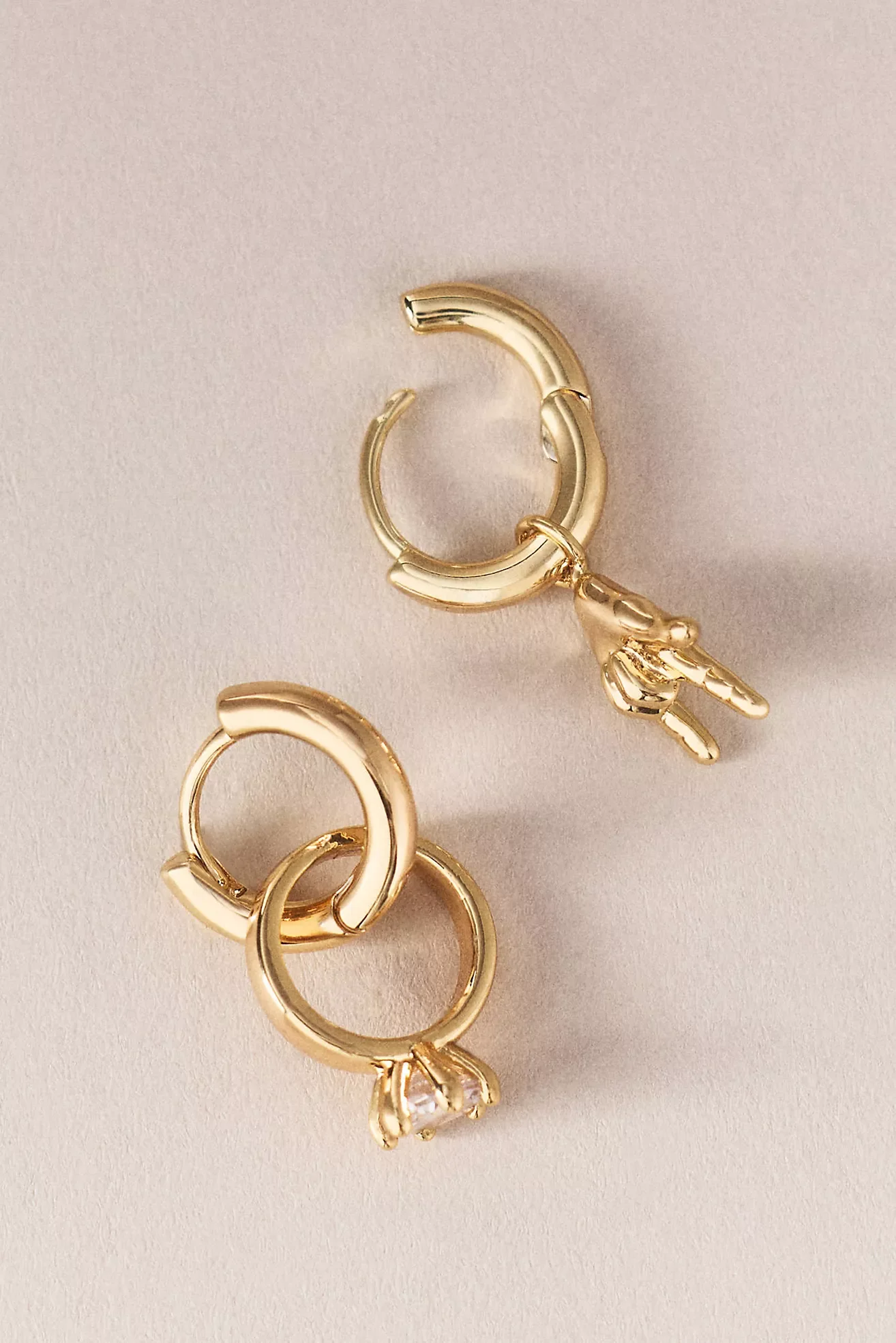 Close-up of gold hoop earrings with small charms, including a triangle-shaped stone, on a light pink background.