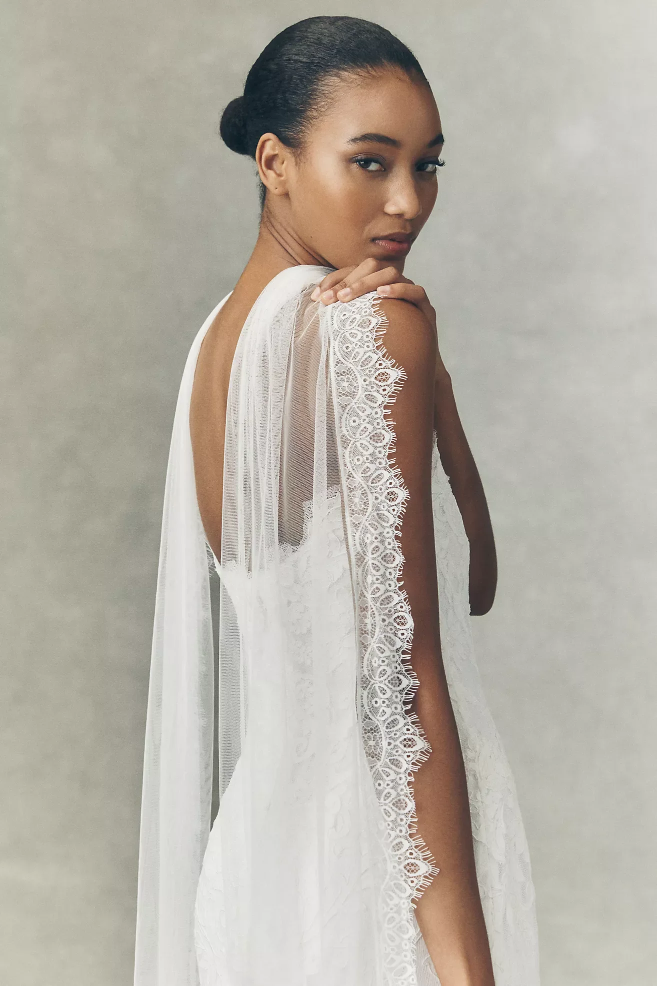 A woman with dark hair styled in an elegant updo, wearing a white lace robe with intricate lace trim details.