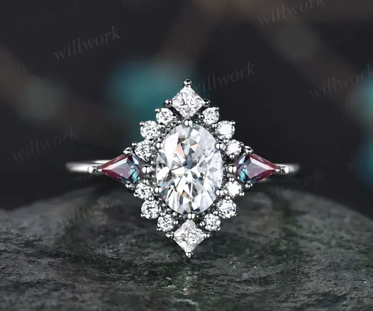 A silver ring with a large oval-cut diamond surrounded by smaller diamonds and pink gemstones, set on a dark surface.