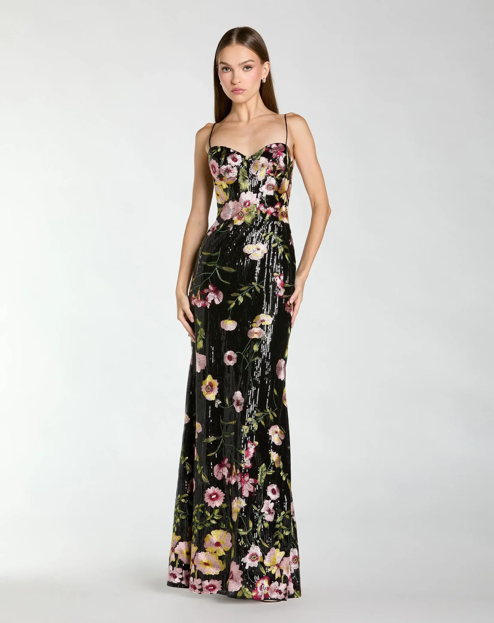 A young woman with long brown hair wearing a sleeveless black dress with a floral pattern.