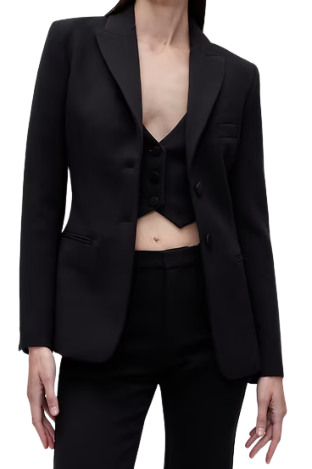 Woman wearing a black tailored blazer, black crop top, and black pants, with a visible navel piercing.