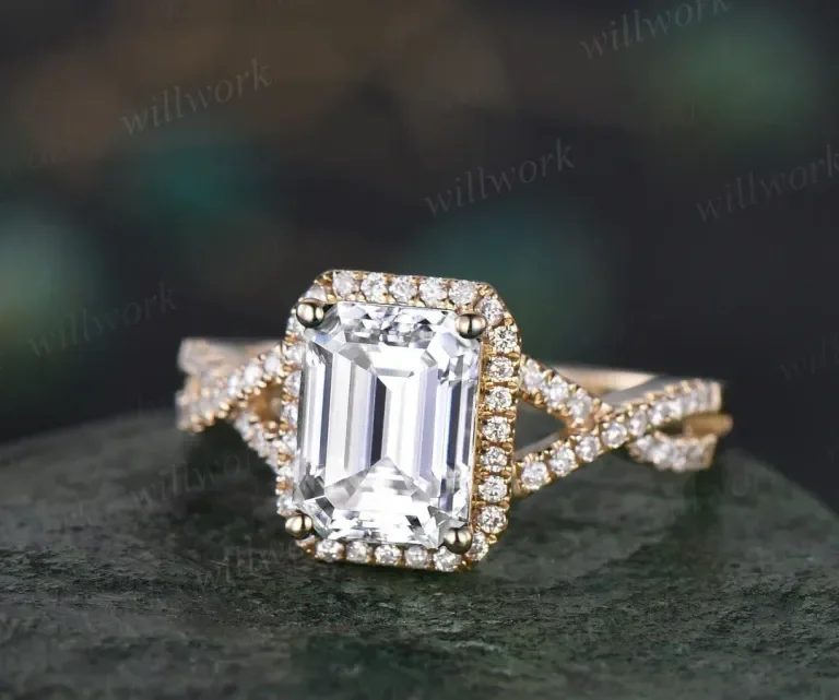 A gold ring with a large emerald-cut diamond in the center, surrounded by smaller diamonds, resting on a dark surface.