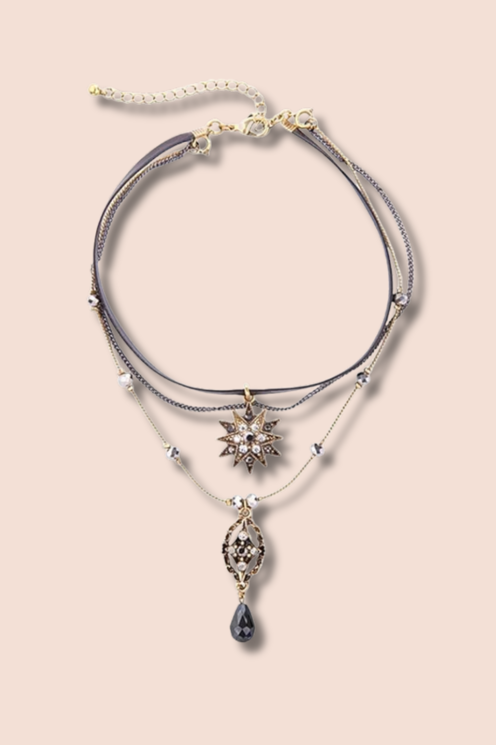 Layered gold and silver necklaces with star and teardrop pendants on a light pink background.