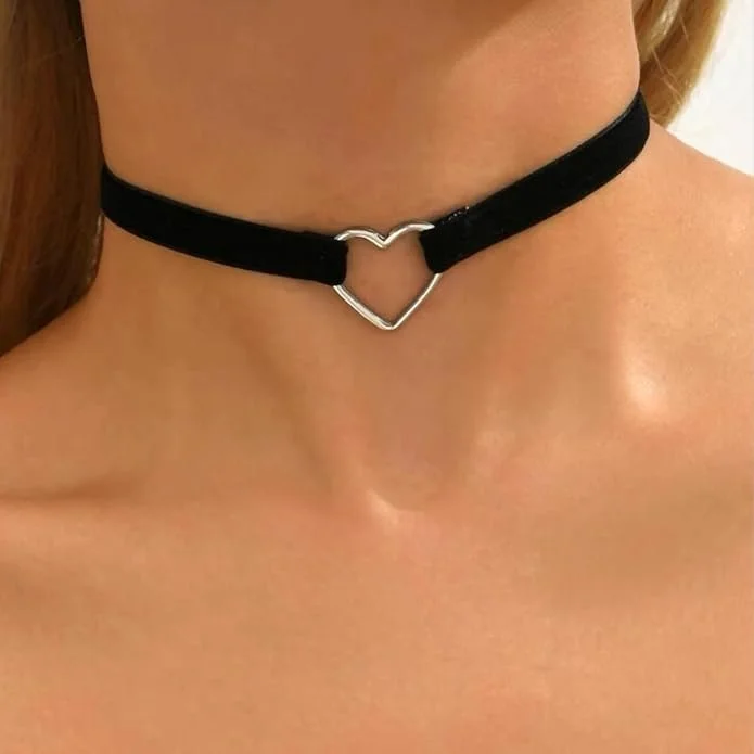 Close-up of a person's neck and collarbone area, wearing a black choker with a silver heart-shaped pendant.