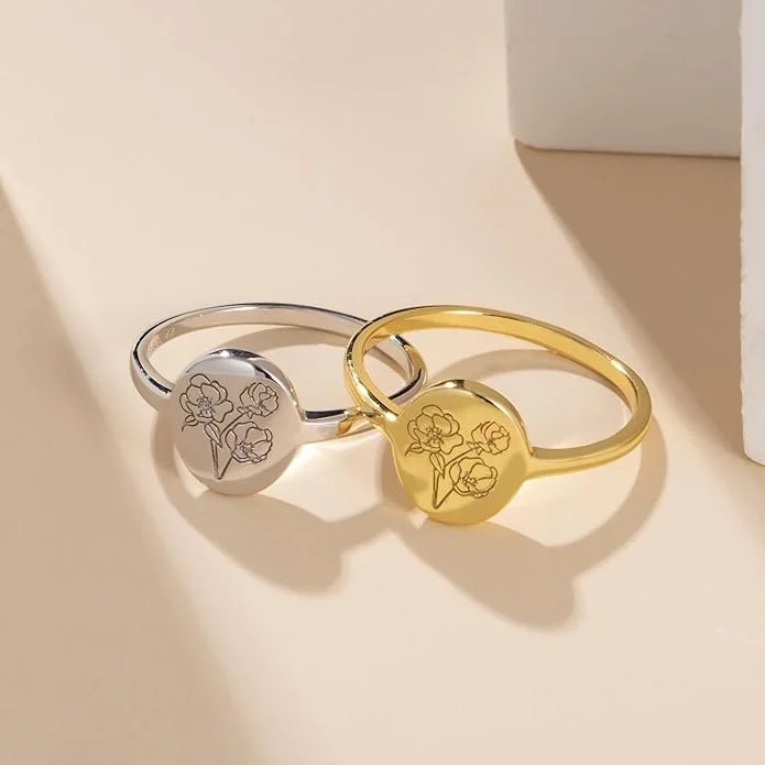 Two rings, one silver and one gold, with floral engravings on the top surfaces, placed on a light-colored surface.