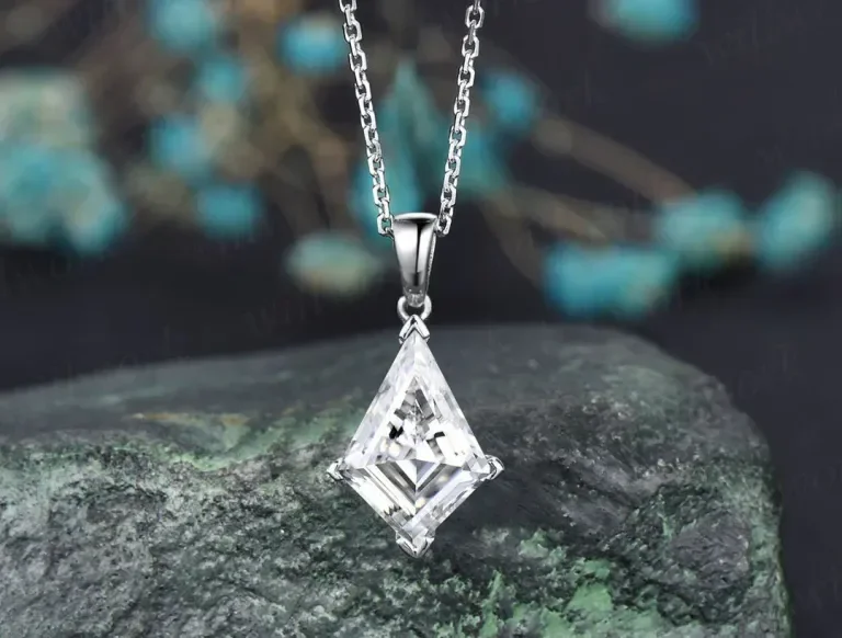 Silver necklace with a large, clear, geometric-shaped crystal pendant resting on a textured, dark green stone.